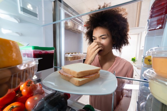 Young Woman Felling Bad Smell From Ham Sandwich Near Refrigerator At Home