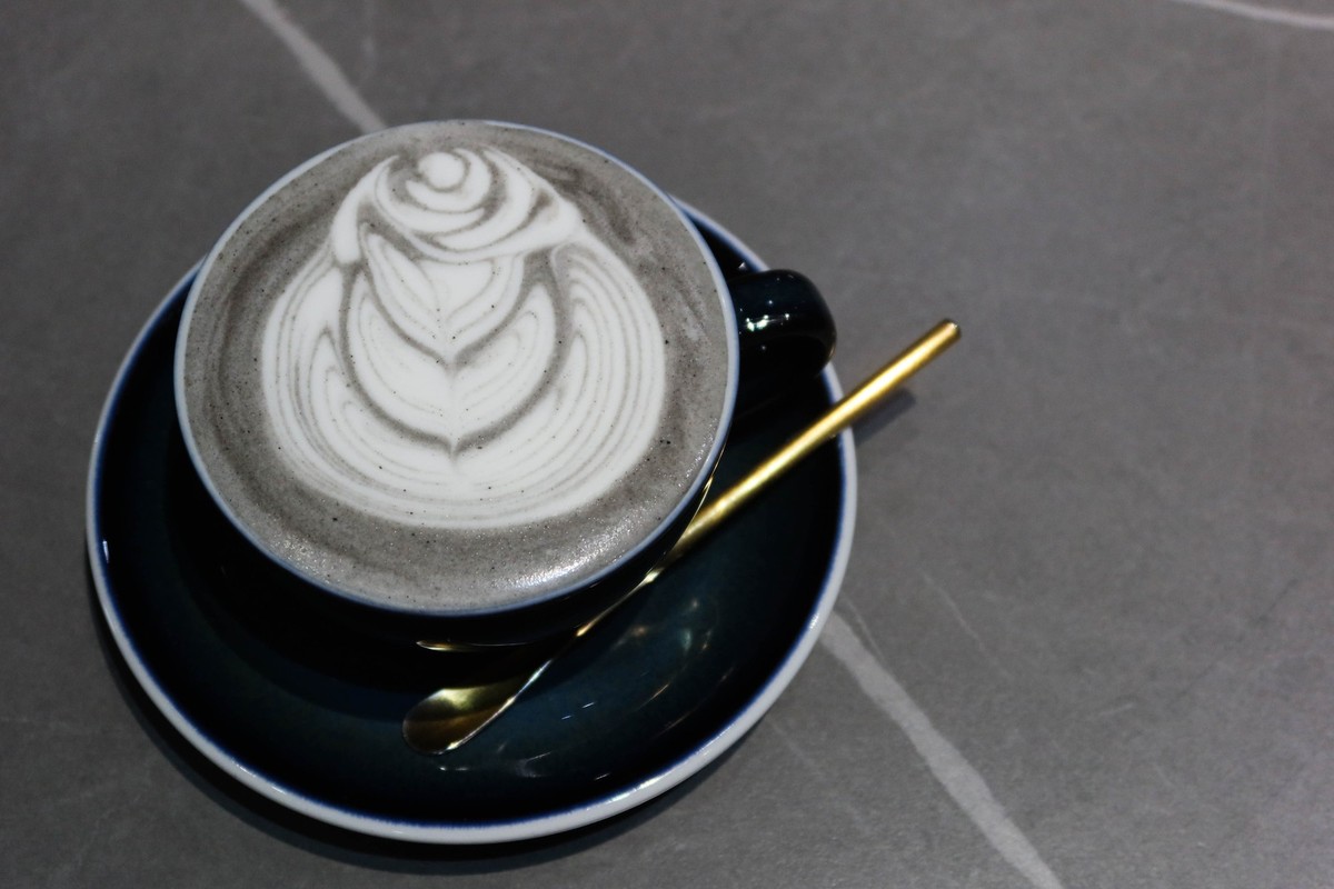 close up of hot gray black sesame latte with cafe art on a grey background with copy space