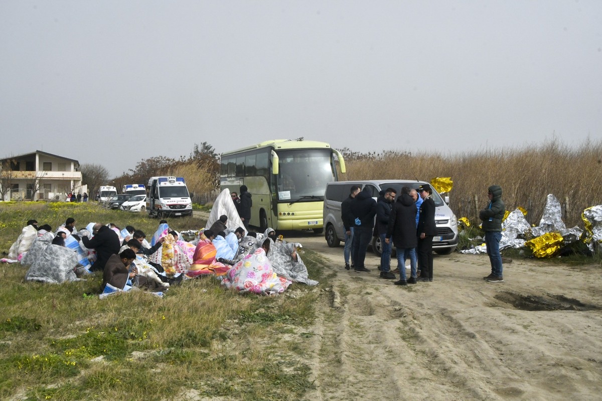 dpatopbilder - 26.02.2023, Italien, Cutro: Gerettete Migranten sitzen in Decken gehüllt an einem Strand in der Nähe von Cutro. Bei einem Bootsunglück mit Migranten an der süditalienischen Küste sind M ...
