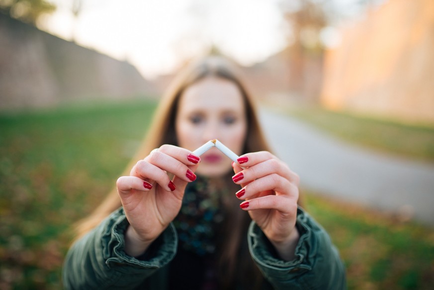 Quit Smoking. Closeup Of Beautiful Girl Holding Broken Cigarette In Hands. Portrait Of Smiling Young Woman Breaking Cigarette In Half, Quitting To Smoke Cigarettes.