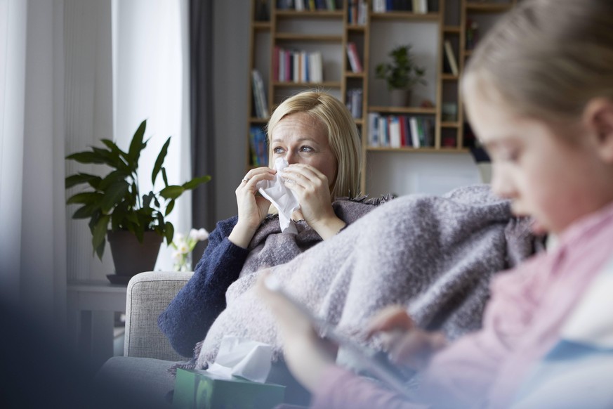 Mother sitting on couch, having a cold, daughter playing in foreground model released Symbolfoto property released PUBLICATIONxINxGERxSUIxAUTxHUNxONLY RBF06276