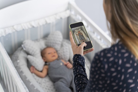 Young mother taking a photo of her newborn baby in the crib in the bedroom
