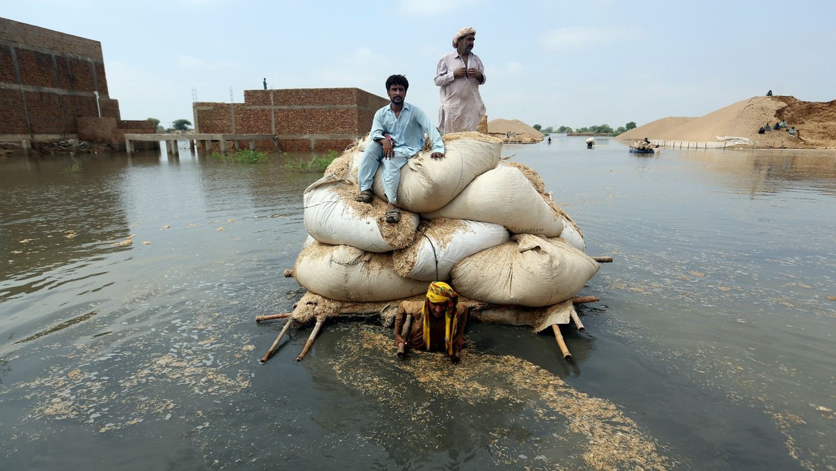 ARCHIV - 05.09.2022, Pakistan, Jaffarabad: Anwohner befördern Säcke mit Futter für ihr Vieh auf einem behelfsmäßigen Floß durch das Hochwasser nach heftigen Monsunregen. Foto: Fareed Khan/AP/dpa +++ d ...