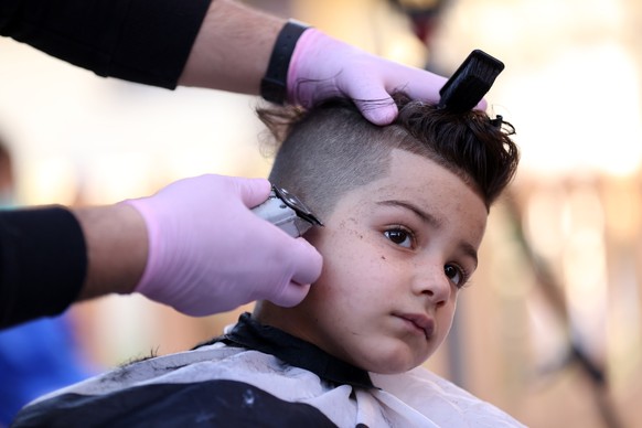 BAGHDAD, IRAQ - APRIL 10: Barber Seyf Casim (26), wearing gloves and a face mask, gives a child a haircut in eastern Baghdad&#039;s al-Talbiyah area in Iraq on April 10, 2020, amid the coronavirus (CO ...