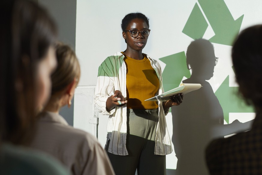 Portrait of young African-American woman giving speech on recycling and waste management during eco conference