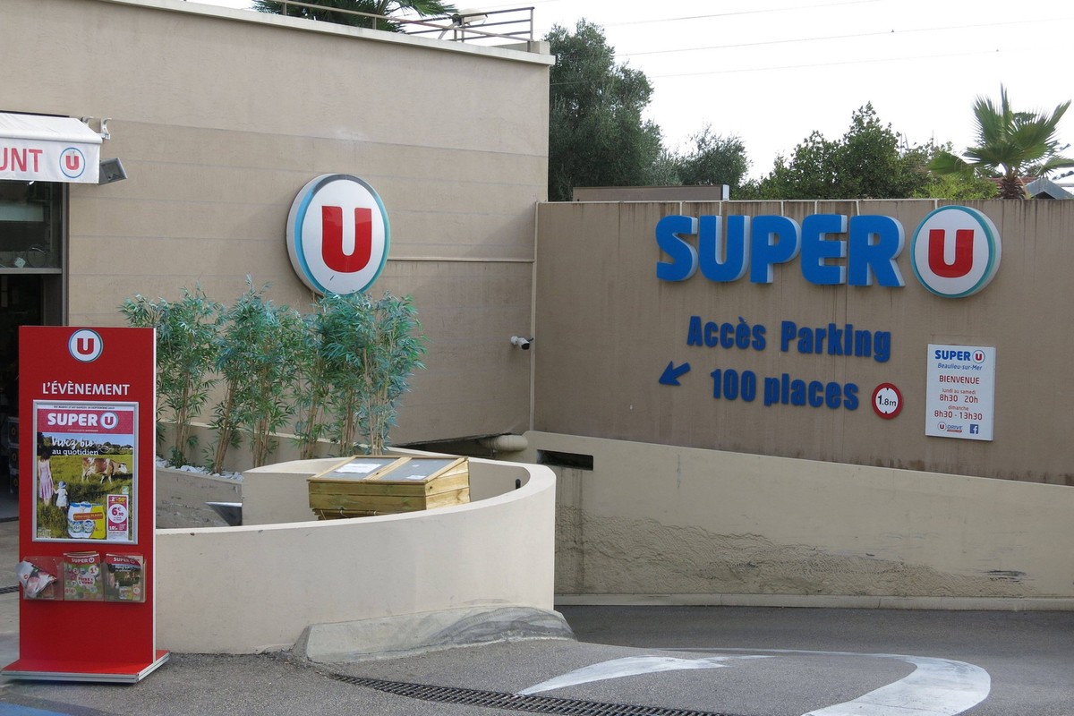 Prospektaufsteller und Zufahrt zum Parkplatz des Super U Supermarkt Systeme U / Cooperative U Enseigne / Magasins U, Supermarktkette, Nahversorger, Einzelhandel, Lebensmitteleinzelhandel, Logo / Leuch ...