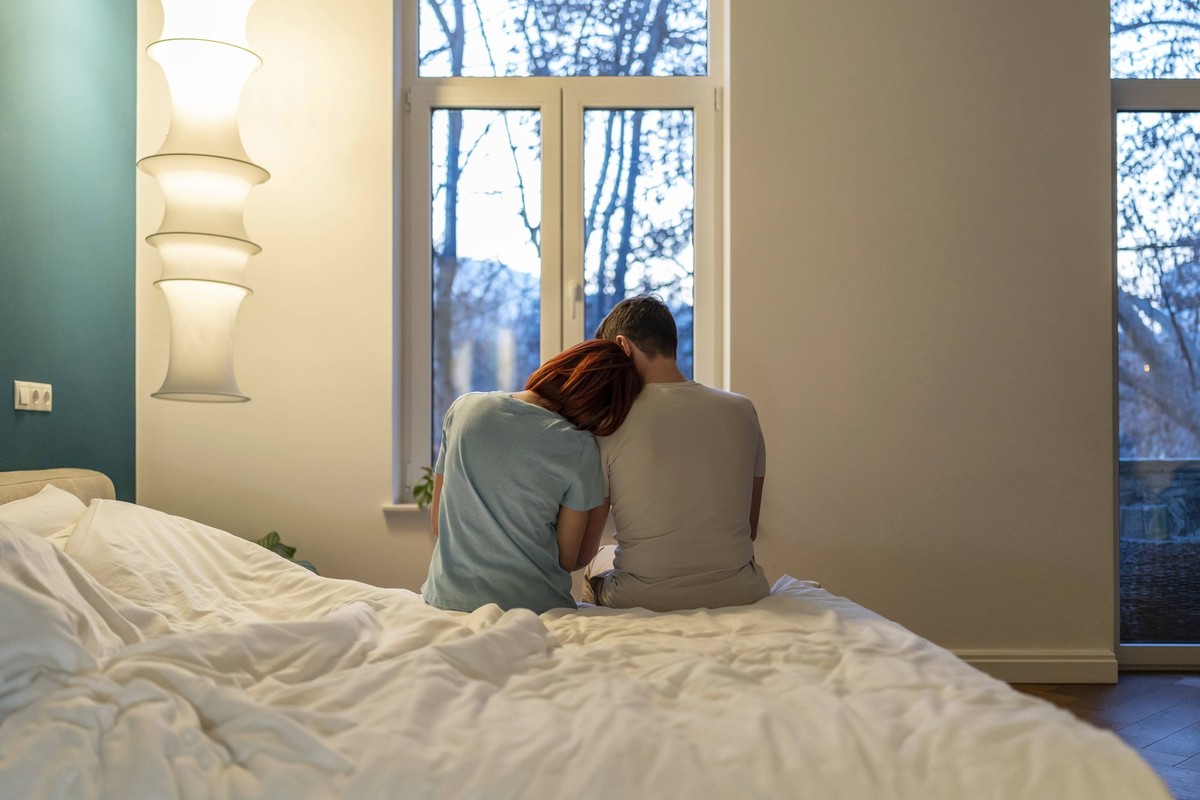 Familie Paar Mann und Frau sitzen zusammen im Bett umarmen Blick auf Fenster im Schlafzimmer zu Hause, Rückansicht. Zärtliche Beziehung, glückliche Ehe, Unterstützung emotionale Hilfe von Lebenspartne ...