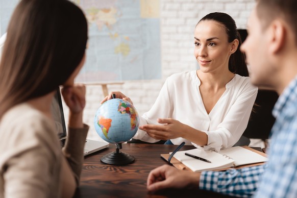 A young man and a woman came to the travel agency. They want to go on a trip during their holidays. The girl agent offers them different countries. She shows it on the globe.