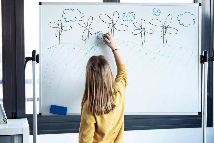 Shot of little girl drawing a eolic park on a whiteboard with a marker pen at home.