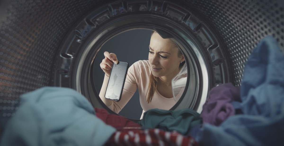 Disappointed woman finding her phone in the washing machine, the phone is damaged and dripping water