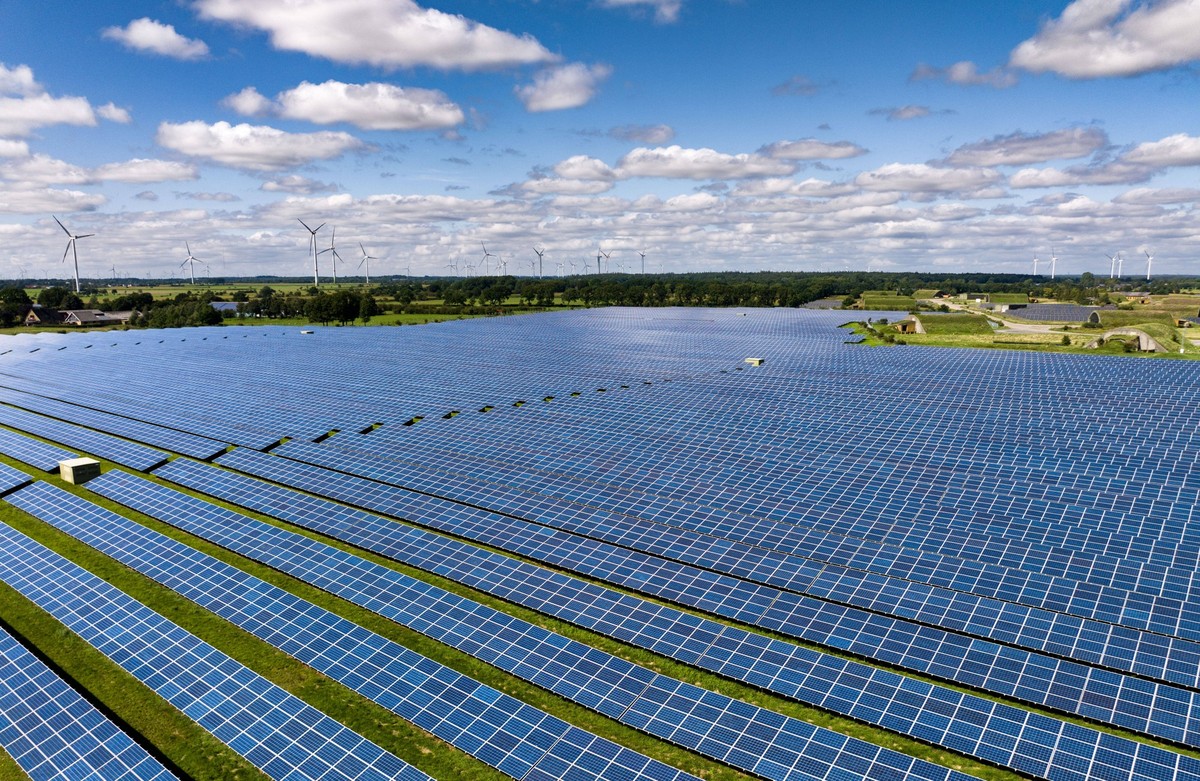 Solarenergie Solarmodule stehen in Reihen in einem Solarkraftwerk. Die Photovoltaik-Anlage wandelt Sonnenenergie in sauberen elektrischen Strom um. Im Hintergrund sind Windkraftanlagen zu sehen. Eggeb ...