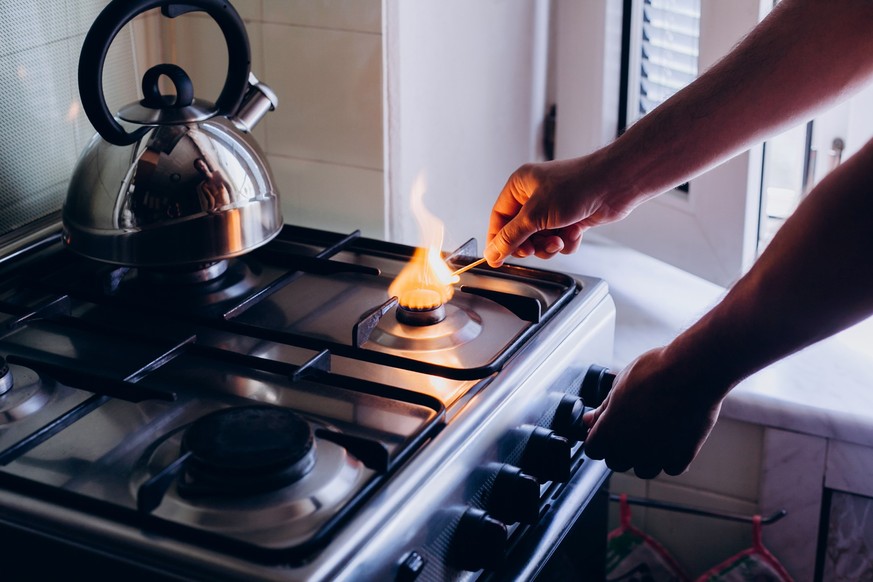 A man&#039;s hand with a match lights a gas burner or a gas stove in the kitchen.