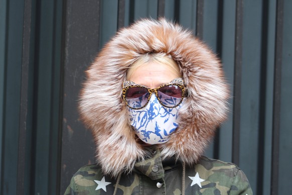 April 16, 2020, New York, New York, USA: This resident in khaki jacket, head covered by a hood lined with fur framing her face, wears a fabric mask covered by wide sunglasses in Manhattan. A new execu ...