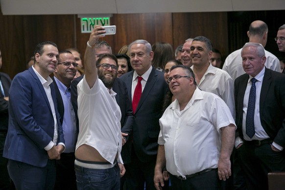 A Knesset member Oren Hazan takes a selfie with Israel&#039;s Prime Minister Benjamin Netanyahu, center, and MP David Bitan, right of Netanyahu, after a Knesset session that passed of a contentious bi ...