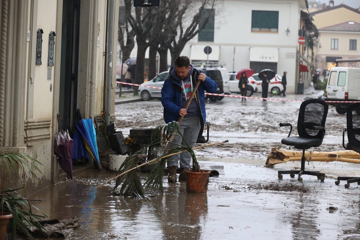 14.03.2025, Italien, Florenz: Ein Mann reinigt eine schlammbedeckte Stra