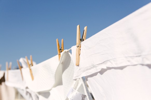White clothes hung out to dry on a washing line in the bright warm sun. Background is a clear blue sky. Wäscheleine
