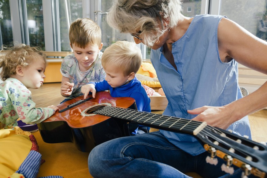 Pre-school teacher showing a guitar to children in kindergarten model released Symbolfoto property released PUBLICATIONxINxGERxSUIxAUTxHUNxONLY MFF04096