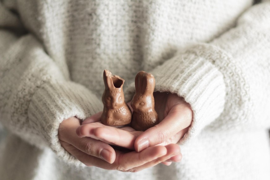 Woman hands holding two chocolate Easter rabbits, one with a bite