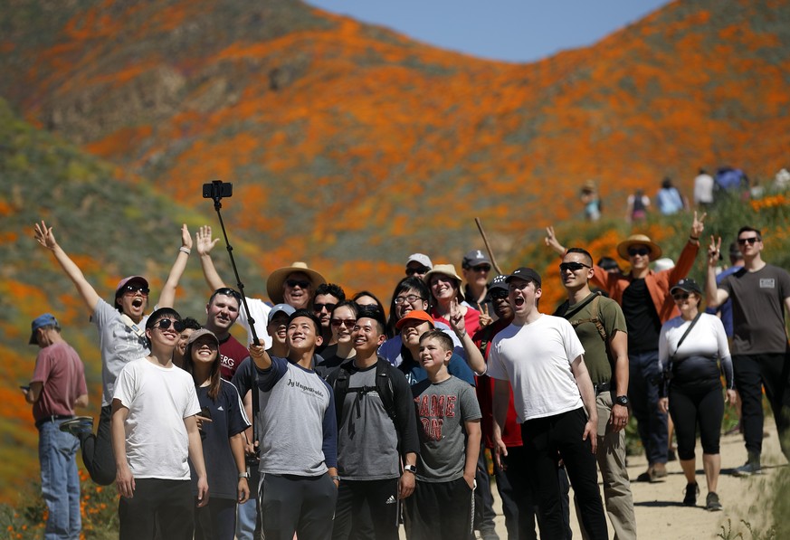 People pose for a picture among wildflowers in bloom Monday, March 18, 2019, in Lake Elsinore, Calif. About 150,000 people flocked over the weekend to see this year&#039;s rain-fed flaming orange patc ...