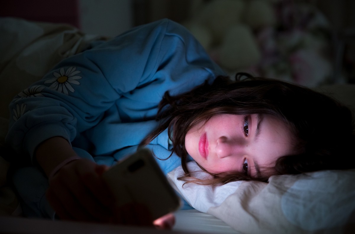 A child using smart phone lying in bed late at night, playing games, watching videos online, scrolling screen. Children&#039;s screen addiction. Child&#039;s room at night.