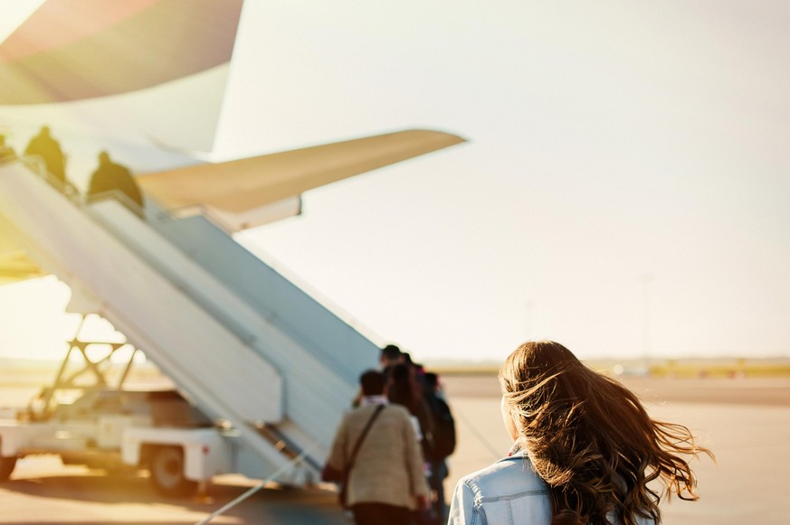 Woman tourist passenger getting in to airplane at airport, walking from the terminal to the plane.