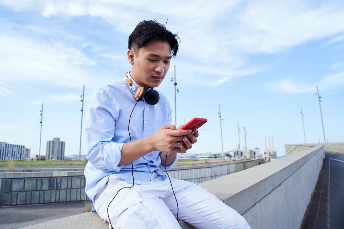 Concentrated Asian young man using cell phone outdoors. Serious Chinese boy texting on his smart phone. People communicating chatting online apps. One male person addicted to technology.
