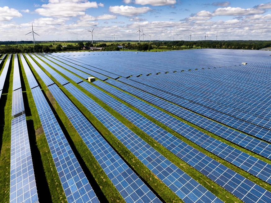 Solarenergie Solarmodule stehen in Reihen in einem Solarkraftwerk. Die Photovoltaik-Anlage wandelt Sonnenenergie in sauberen elektrischen Strom um. Im Hintergrund sind Windkraftanlagen zu sehen. Eggeb ...